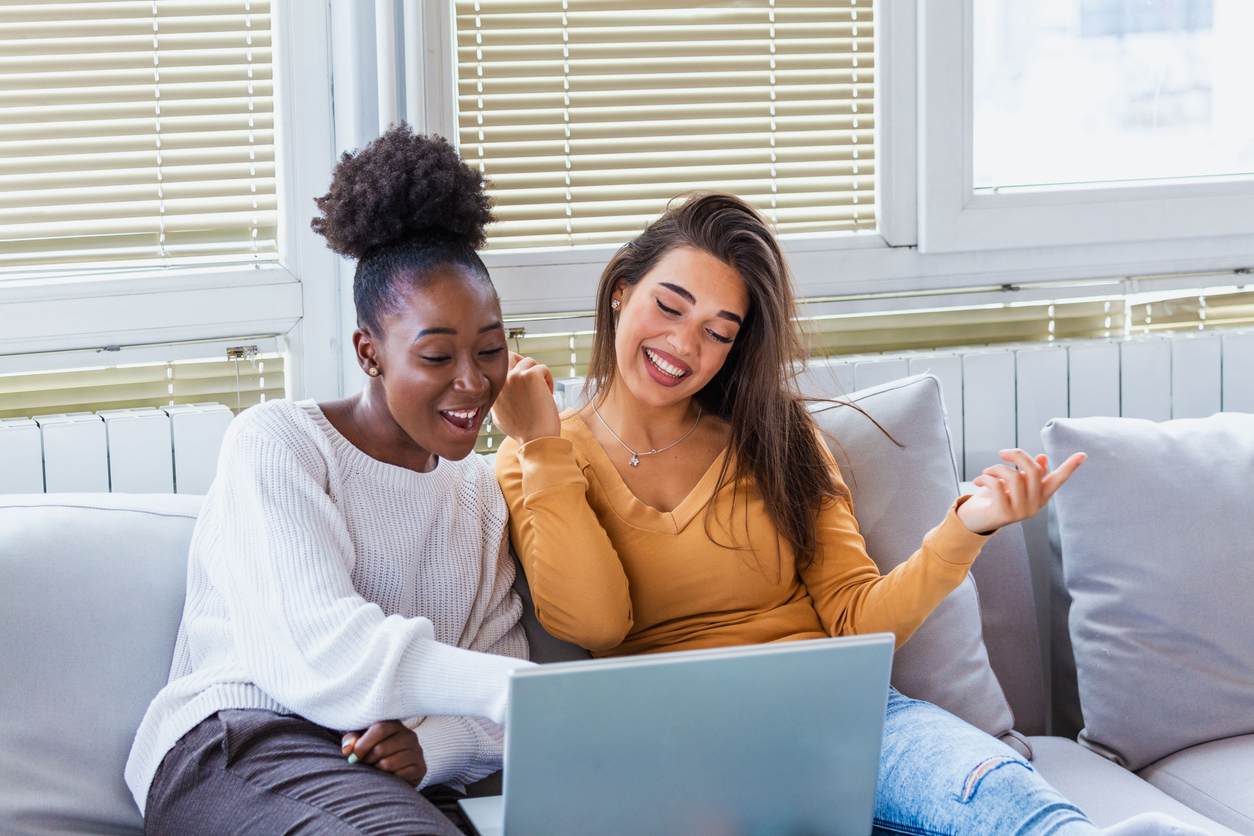 Portrait of a happy girlfriends surfing the net on laptop at home. Lovable Caucasian and African American girls having fun at home stock photo