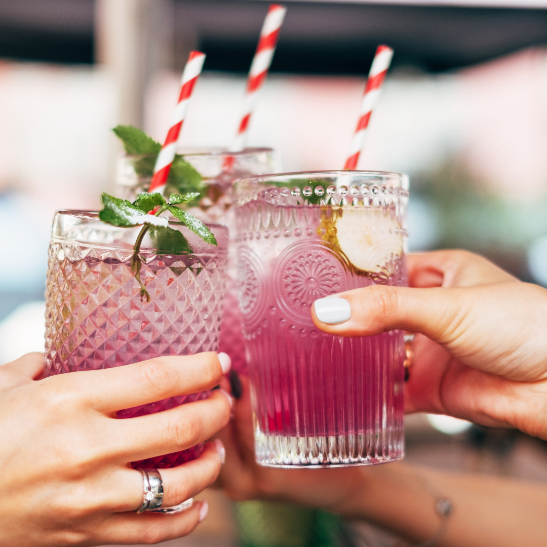 Friends raising a toast with purple cocktails and mocktails with red and white striped straws