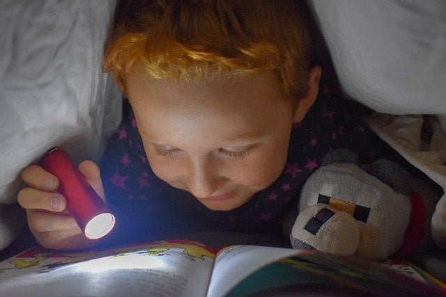 child reading a book with a flashlight