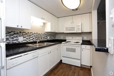 A kitchen with white cabinets and black countertops.