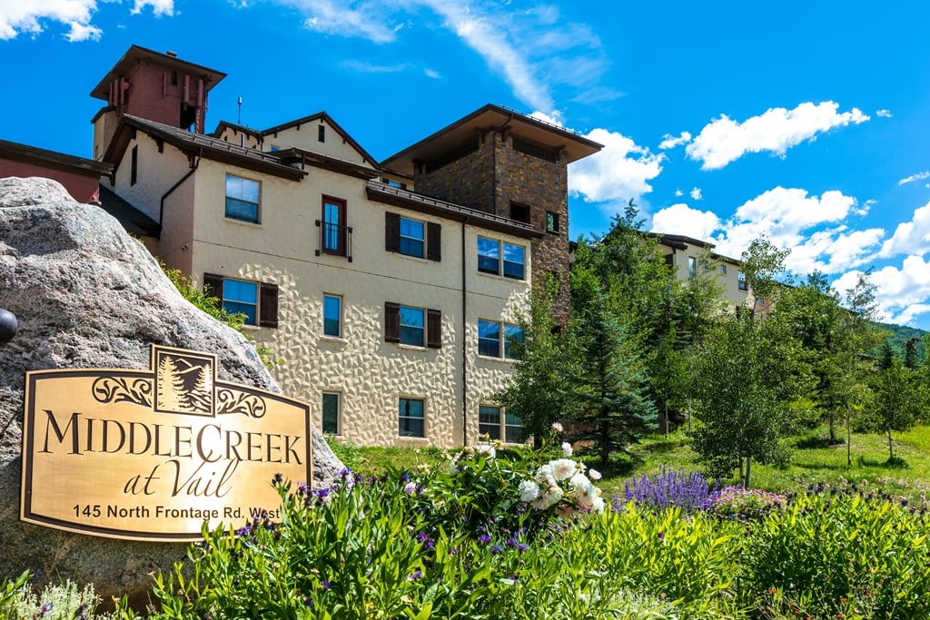 A large rock with a sign that says Middle Creek at Vail in front of a building.