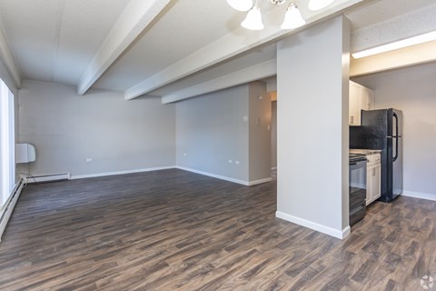 A room with a black fridge and wooden flooring.