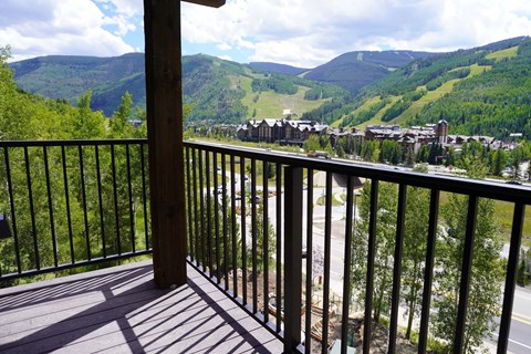 A balcony overlooks a valley with houses and trees.