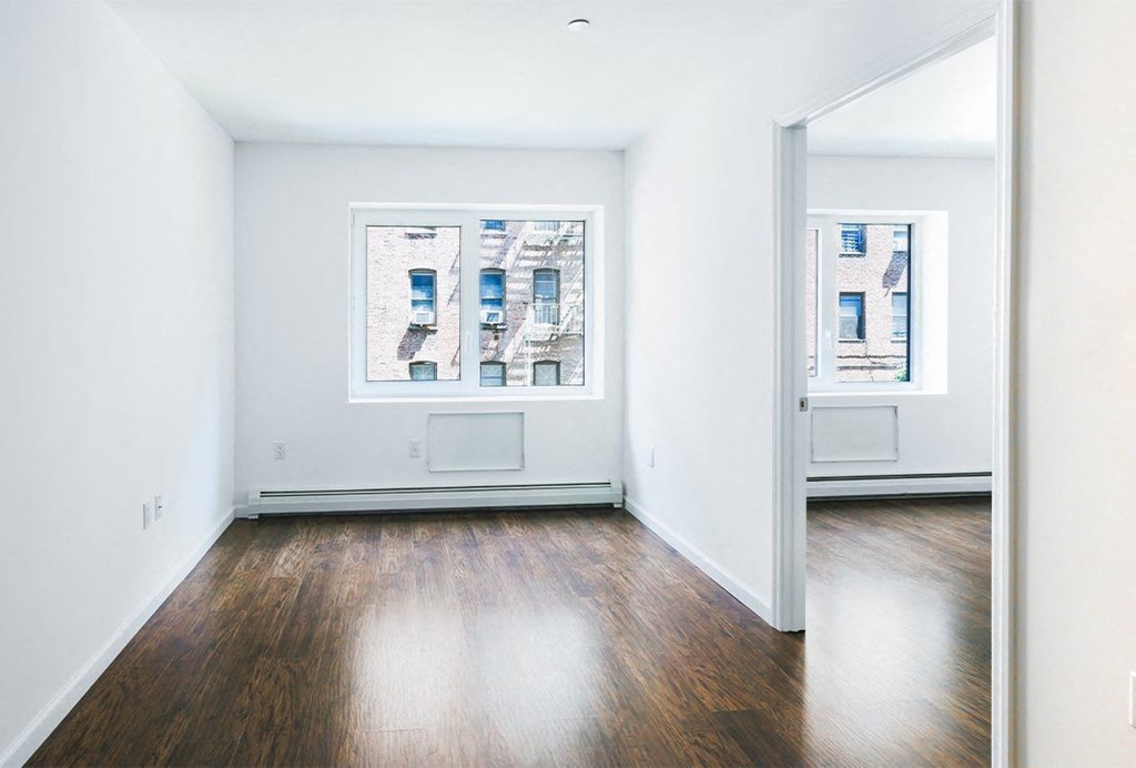 an empty room with wood floors and two windows