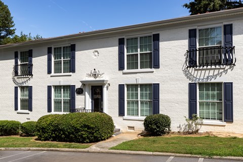 a white brick building with black window shutters and a lawn