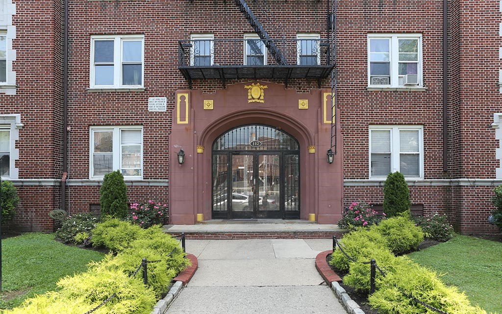 the front door of a brick building with a walkway and grass