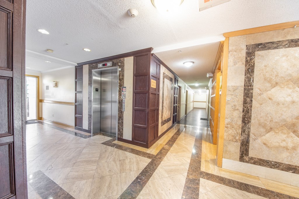 the lobby of a building with a hallway with elevators and marble floors