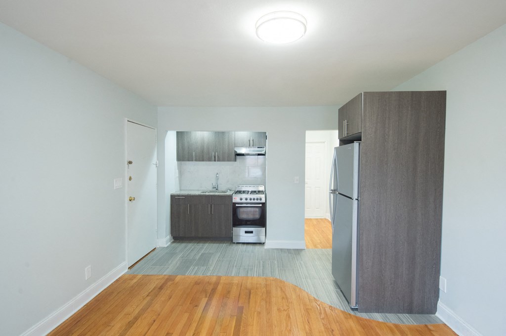 an empty living room with a refrigerator and a kitchen