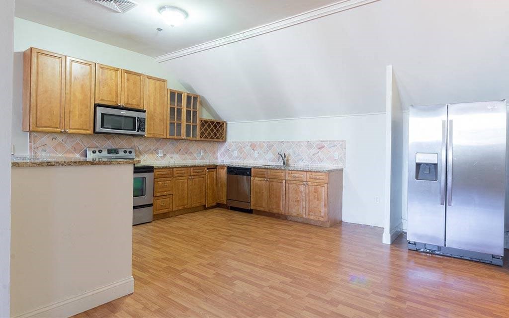 an empty kitchen with wooden cabinets and a stainless steel refrigerator