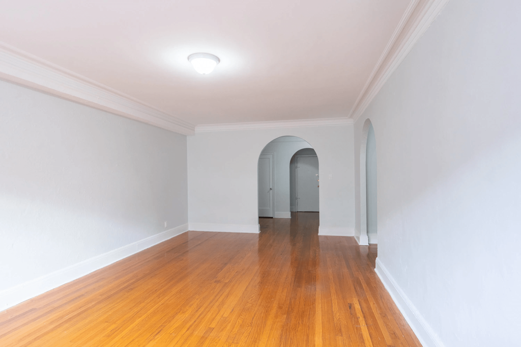 a living room with white walls and a wooden floor and an arched doorway