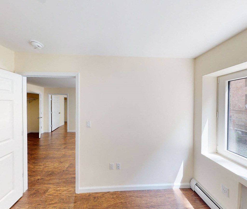 an empty room with a hallway to a bedroom and a window
