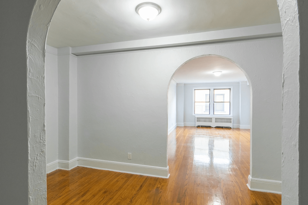 the living room of an empty house with a wooden floor and an arched doorway