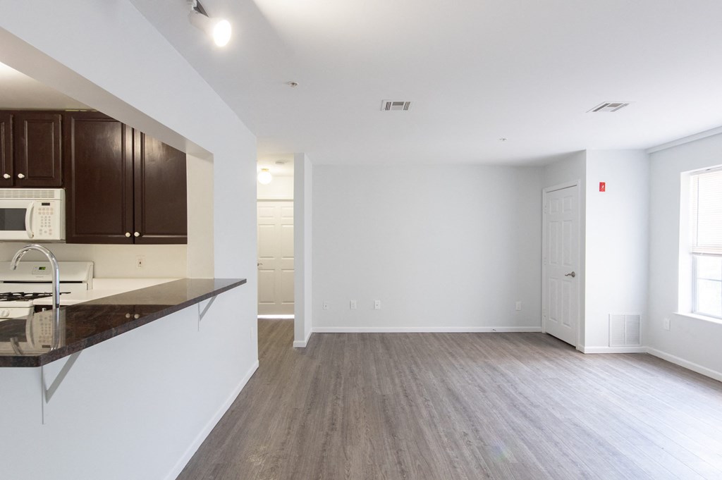 an empty living room and kitchen with white walls and wood flooring