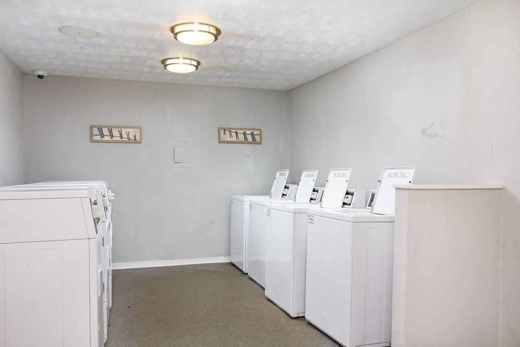 a row of white washers and dryers in an empty room