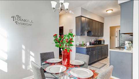 A dining room with a table set for two and a wall decal that says "Be Thankful Everyday".