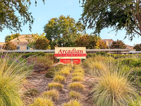 A sign for Arcadian Apartments is in the foreground with a path leading to it.