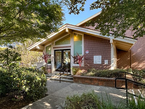 A building with a red brick exterior and a glass door surrounded by greenery.