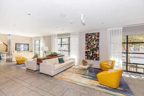 A living room with a white couch, yellow armchair, and a colorful painting on the wall.