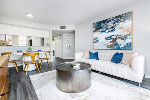 A modern living room with a white couch and a large painting on the wall.