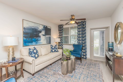 A living room with a white couch, a blue chair, and a painting on the wall.