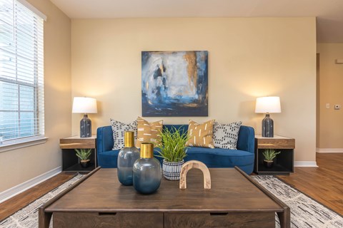 A living room with a blue couch and a painting on the wall.