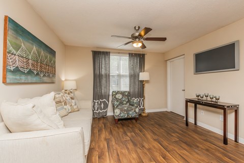 A living room with a white couch, a painting on the wall, a ceiling fan, and a wooden table with candles on it.
