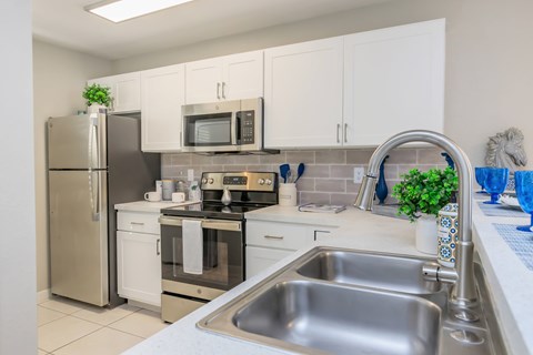 A kitchen with a stainless steel sink and white cabinets.