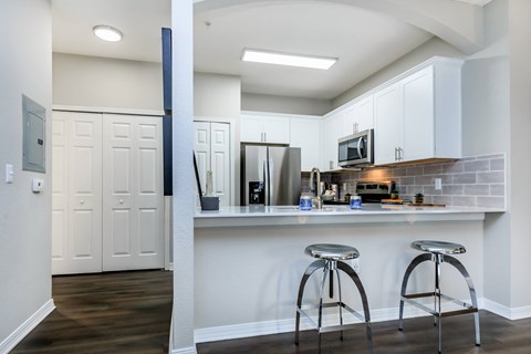 A kitchen with white cabinets and a bar area with stools.