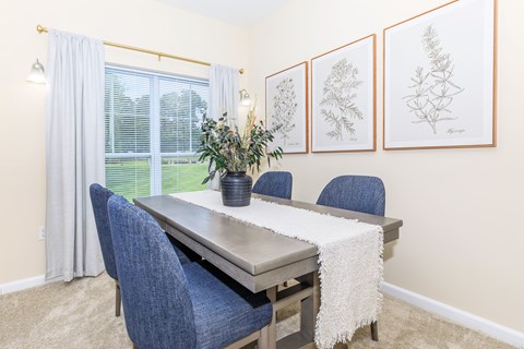 A dining room with a table, chairs, and pictures on the wall.