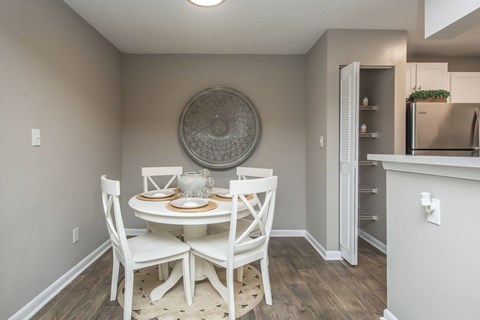 A dining room with a round decorative plate on the wall and a white dining table with four chairs.