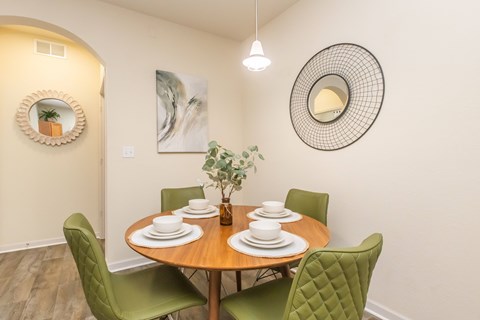 A dining room with a round table and green chairs.