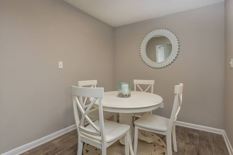 A white table with four chairs and a round mirror on the wall.