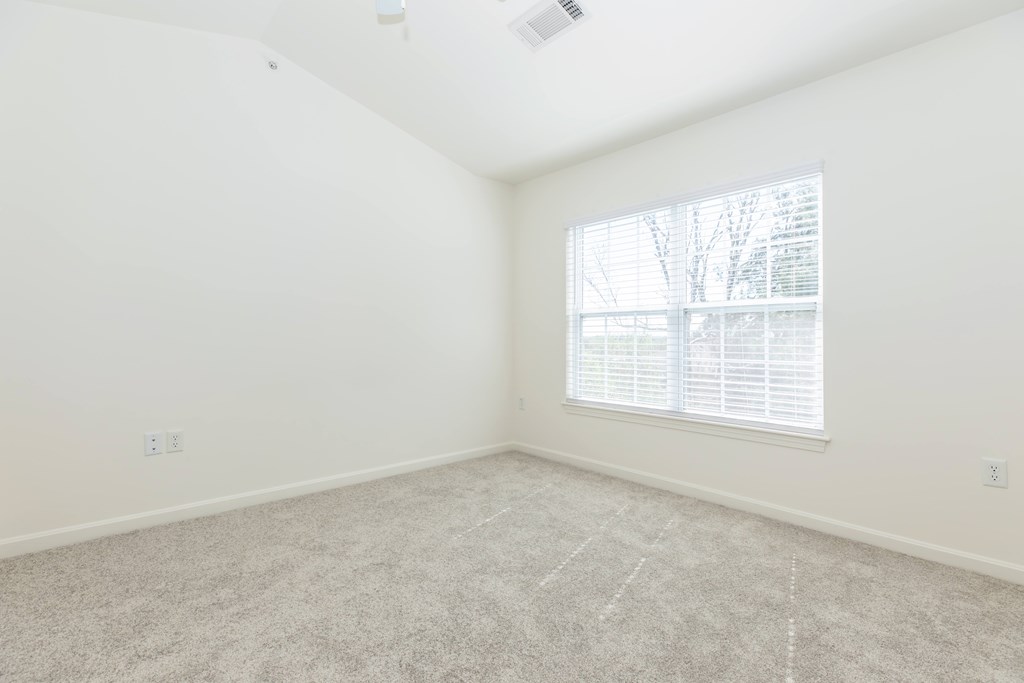 A room with a carpeted floor and a window with blinds.