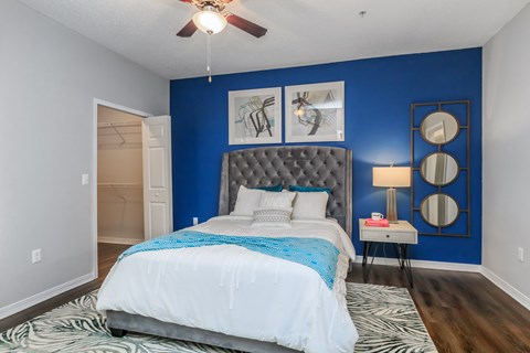 A bedroom with a bed, a ceiling fan, and a nightstand with a lamp.