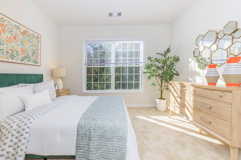 A bedroom with a bed, nightstand, and a plant.