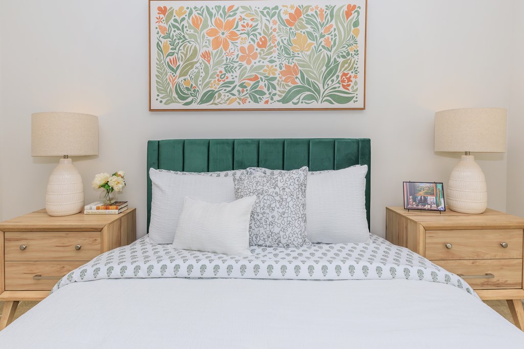 A bedroom with a large bed, a green headboard, and a floral painting on the wall.