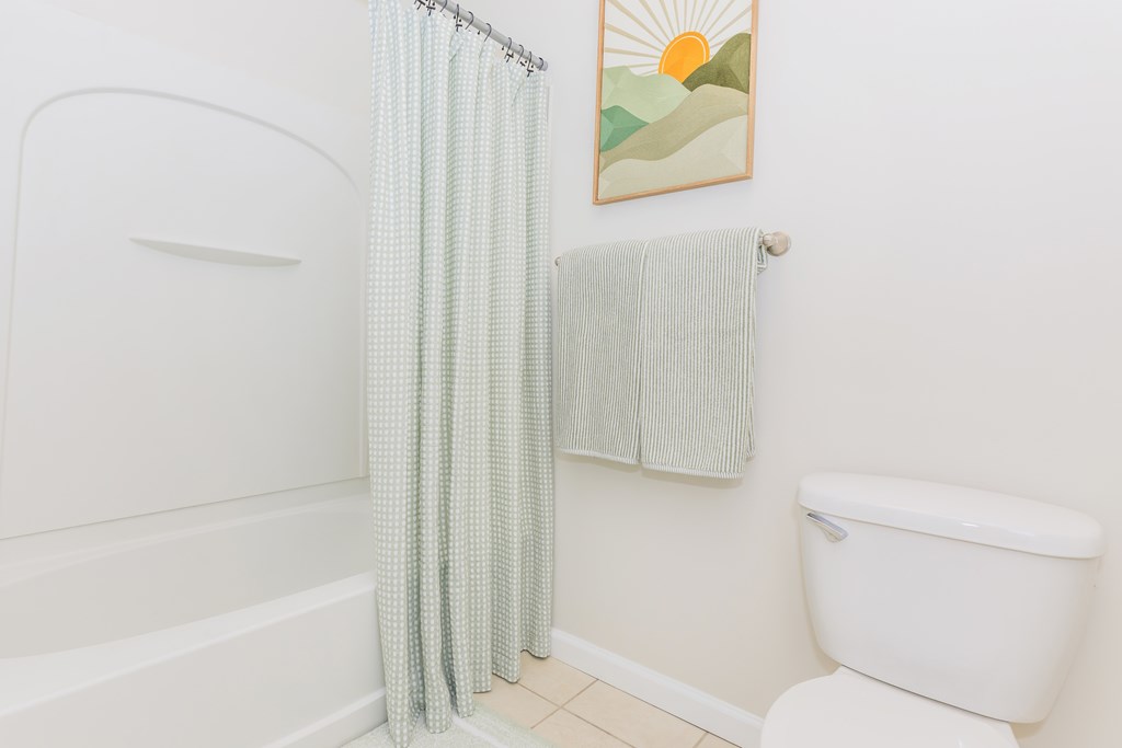 A bathroom with a white tub, toilet, and a shower curtain.