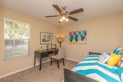 A bedroom with a bed, desk, chair, and a ceiling fan.