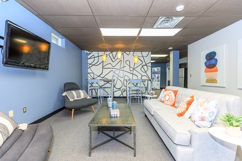 A living room with a grey sofa, a grey armchair, a grey coffee table, and a television on the wall.