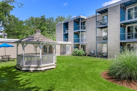 A gazebo is in the middle of a grassy area in front of a building.