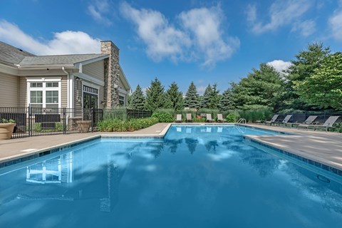 A swimming pool in front of a house with trees in the background.