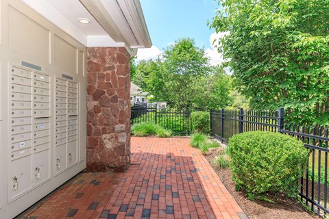 A brick pathway leads to a white building with a black fence and greenery on the side.