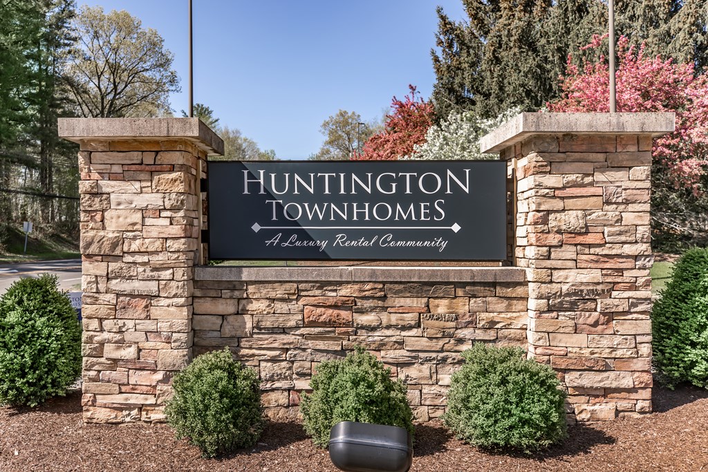 A sign that says Huntington Townhomes stands in front of some trees.