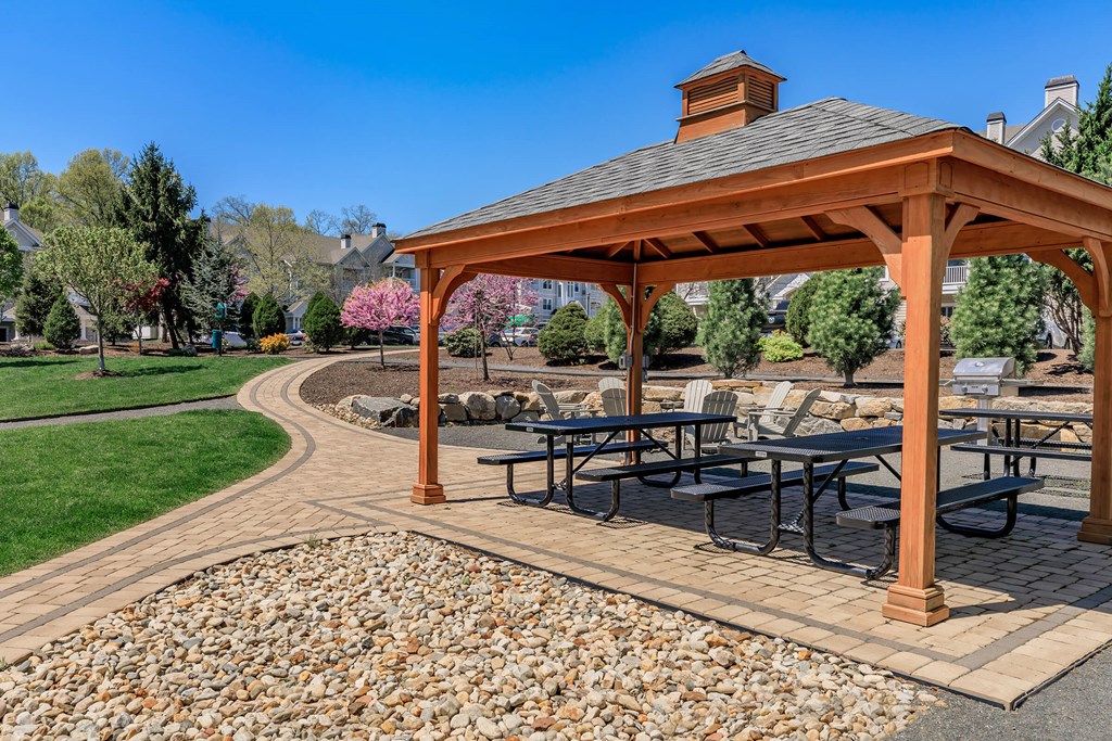 A gazebo with a table and chairs is surrounded by a gravel area and a paved walkway.