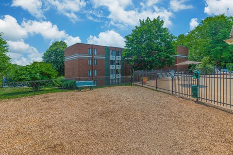 A playground area in front of a brick building with a fence surrounding it.