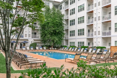 A pool area with sun loungers and a white building in the background.