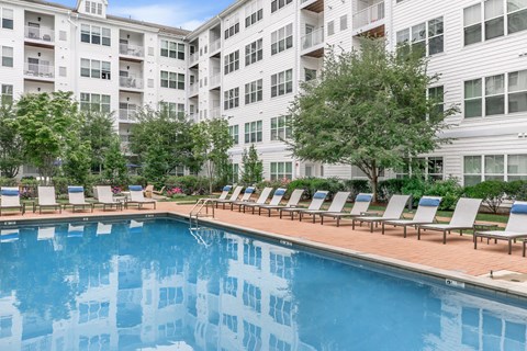A pool with lounge chairs in front of a white building.