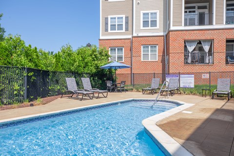 A pool surrounded by chairs and a fence with a building in the background.