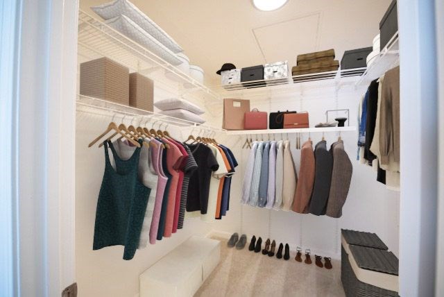 A white closet with clothes hanging and shoes on the floor.