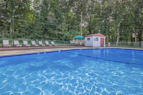 A pool with a red building and sun loungers in the background.